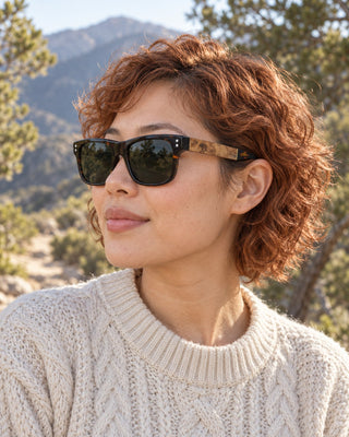 Toro Peak polarized sunglasses worn by a woman among pinyon pines near Toro Peak